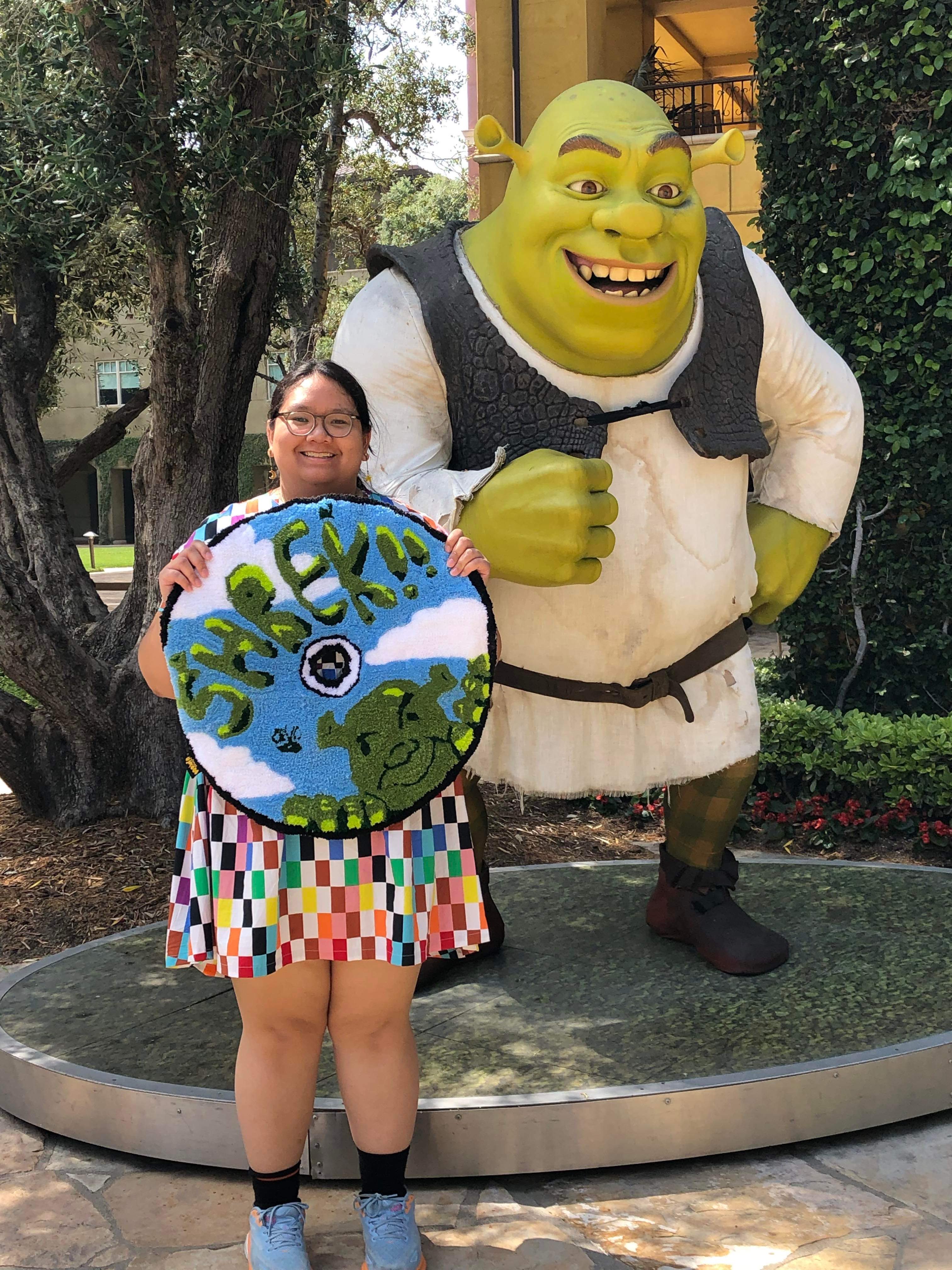 Elie holding a Shrek rug next to a statue of Shrek